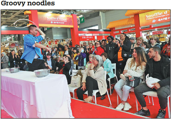 A chef charms visitors with his dance moves as he stretches a thread of noodle during the Paris Fair at Porte de Versailles in Paris, France, on Tuesday. The event was part of a Chinese cultural exhibition at the fair, which started on April 27 and runs through Monday. The fair has attracted more than 3,200 exhibitors from around the world.    Gao Jing / Xinhua